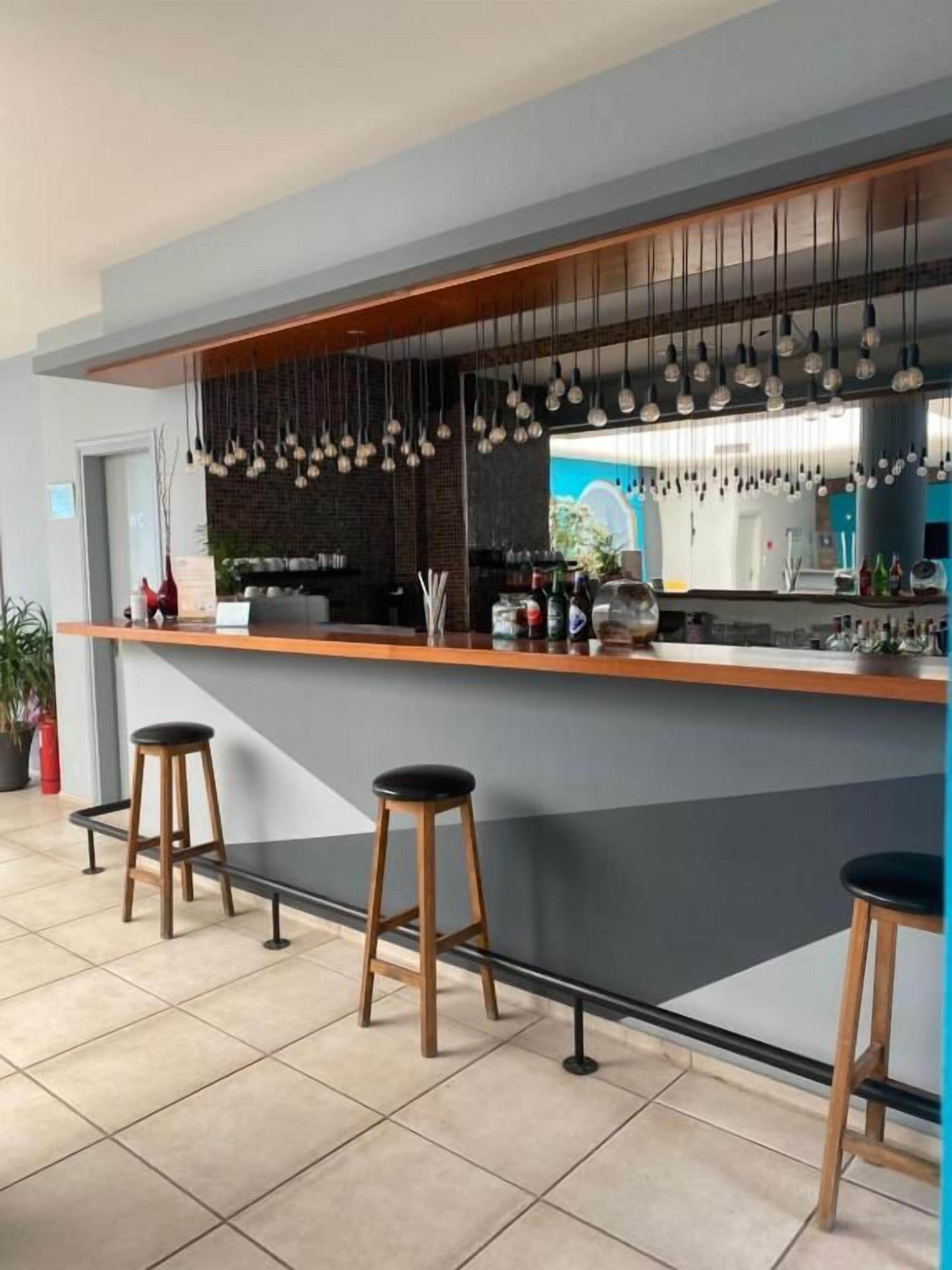Zona de bar con taburetes, una barra, lámparas colgantes y vistas al exterior.
