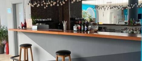 Zona de bar con taburetes, una barra, lámparas colgantes y vistas al exterior.