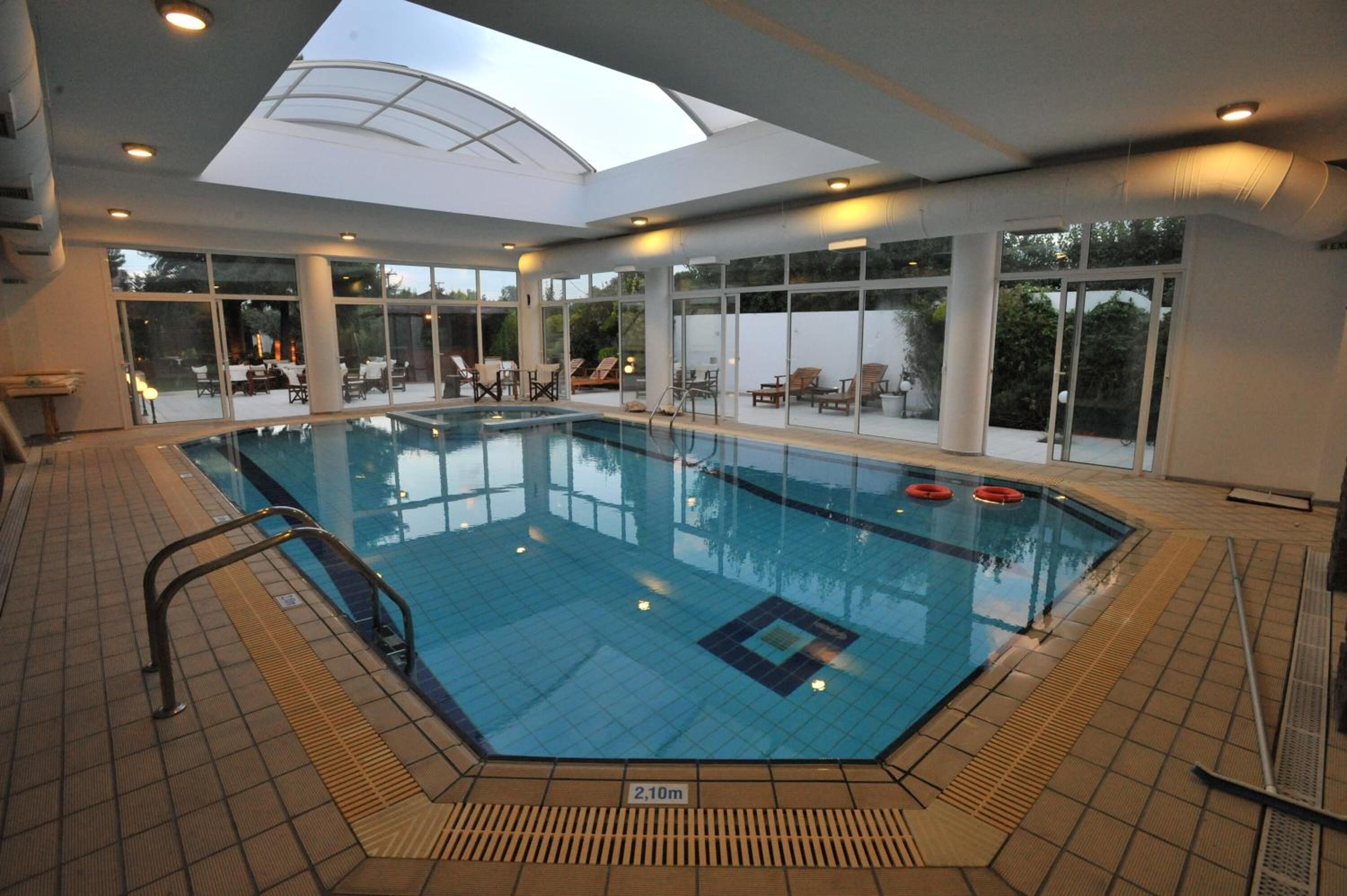 Une piscine intérieure dotée d’une verrière, d’un sol carrelé et de chaises longues disposées autour de la piscine.