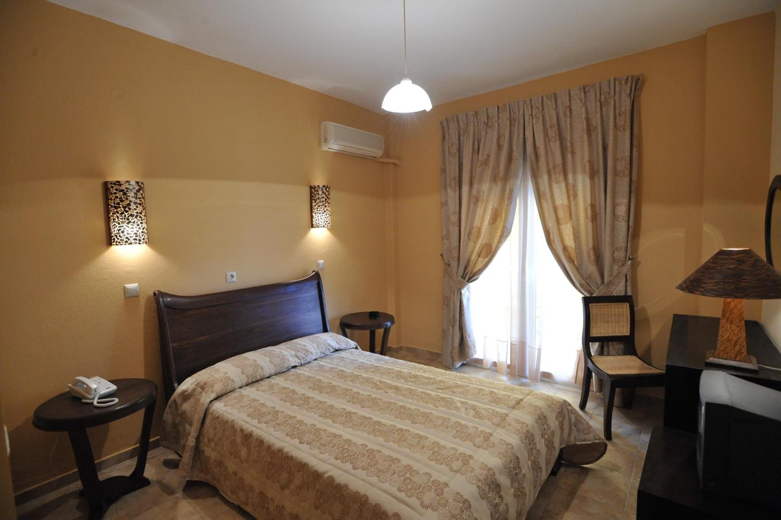 A hotel room with a bed, bedside tables, a desk with a chair, a lamp, and curtains.