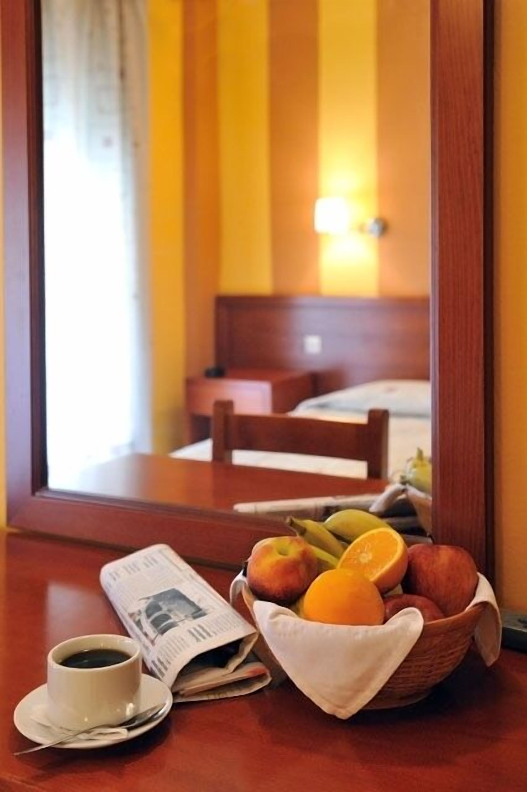 A hotel room with a wooden table, a newspaper, a cup of coffee, and a fruit basket.