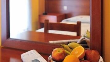 A hotel room with a wooden table, a newspaper, a cup of coffee, and a fruit basket.