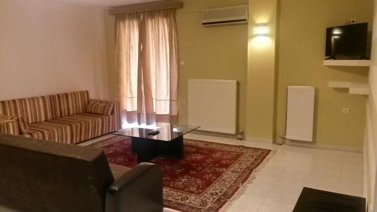 A living room with a striped sofa, a glass coffee table, a red patterned rug, and a TV on a shelf.