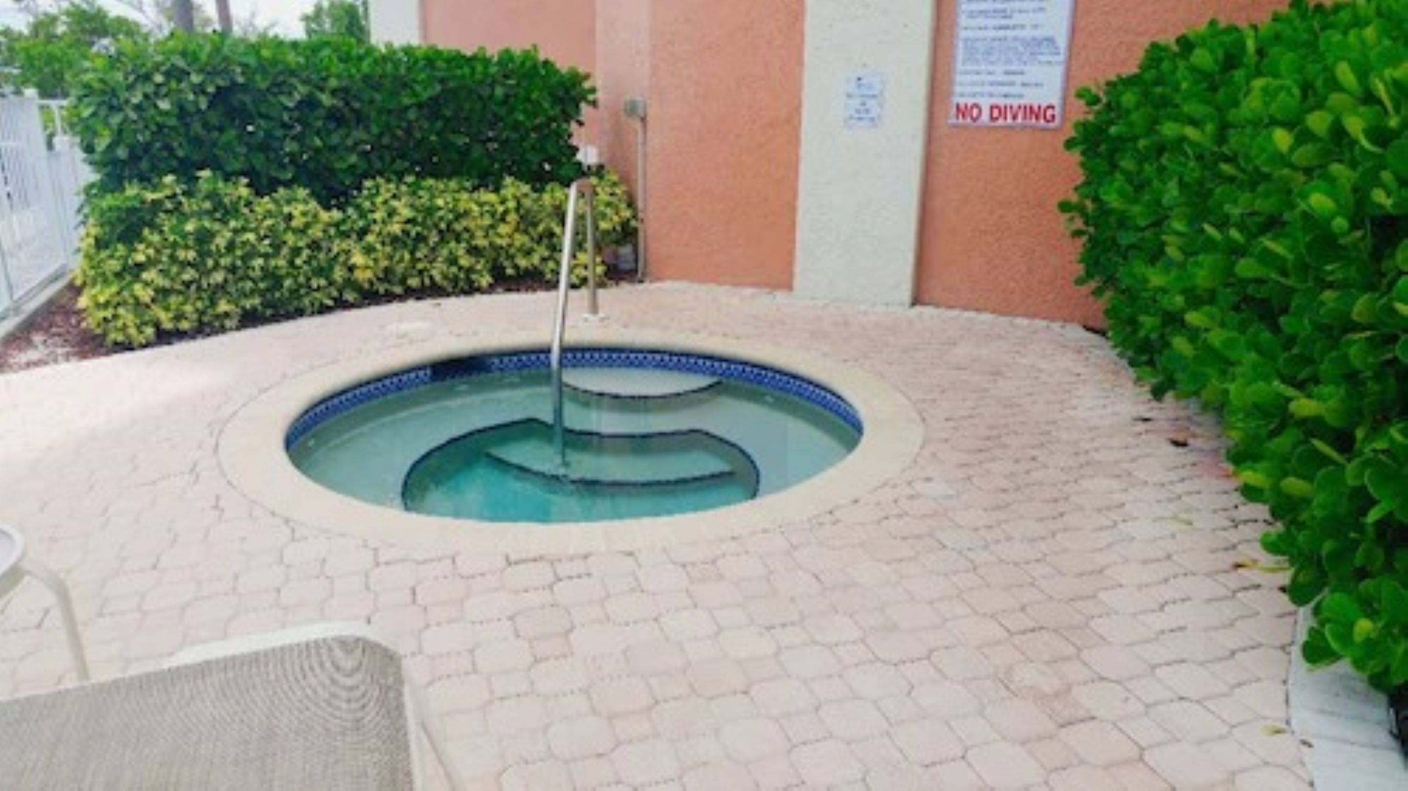 Une piscine avec une fontaine, entourée d’une zone dallée où se trouvent une chaise et une petite table.