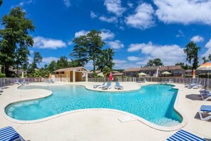A swimming pool with a wavy edge, surrounded by lounge chairs and umbrellas.