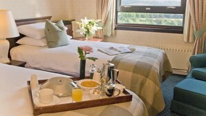 Ein Hotelzimmer mit zwei Betten, einem Frühstückswagen mit Kaffee und Orangensaft und Blick auf Grün hinter dem Fenster.