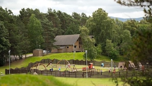 Eine Holzhütte, umgeben von einem Holzzaun, einem Spielplatz und einer Rasenfläche.
