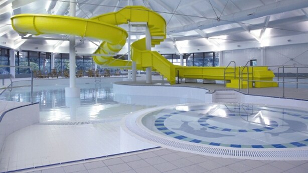 Ein großes Hallenbad mit einer gelben Wasserrutsche und einem kreisförmigen Design auf dem Boden.