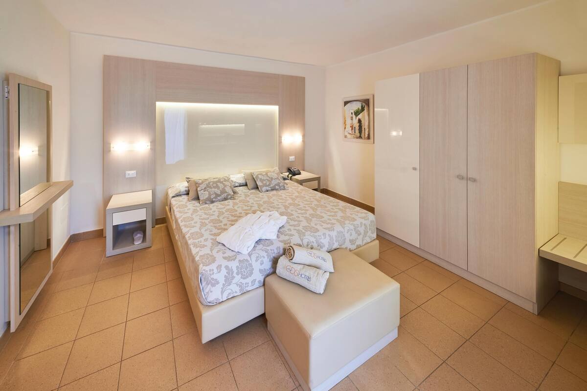 Une chambre d’hôtel avec un grand lit, une table de chevet, une armoire et un miroir.