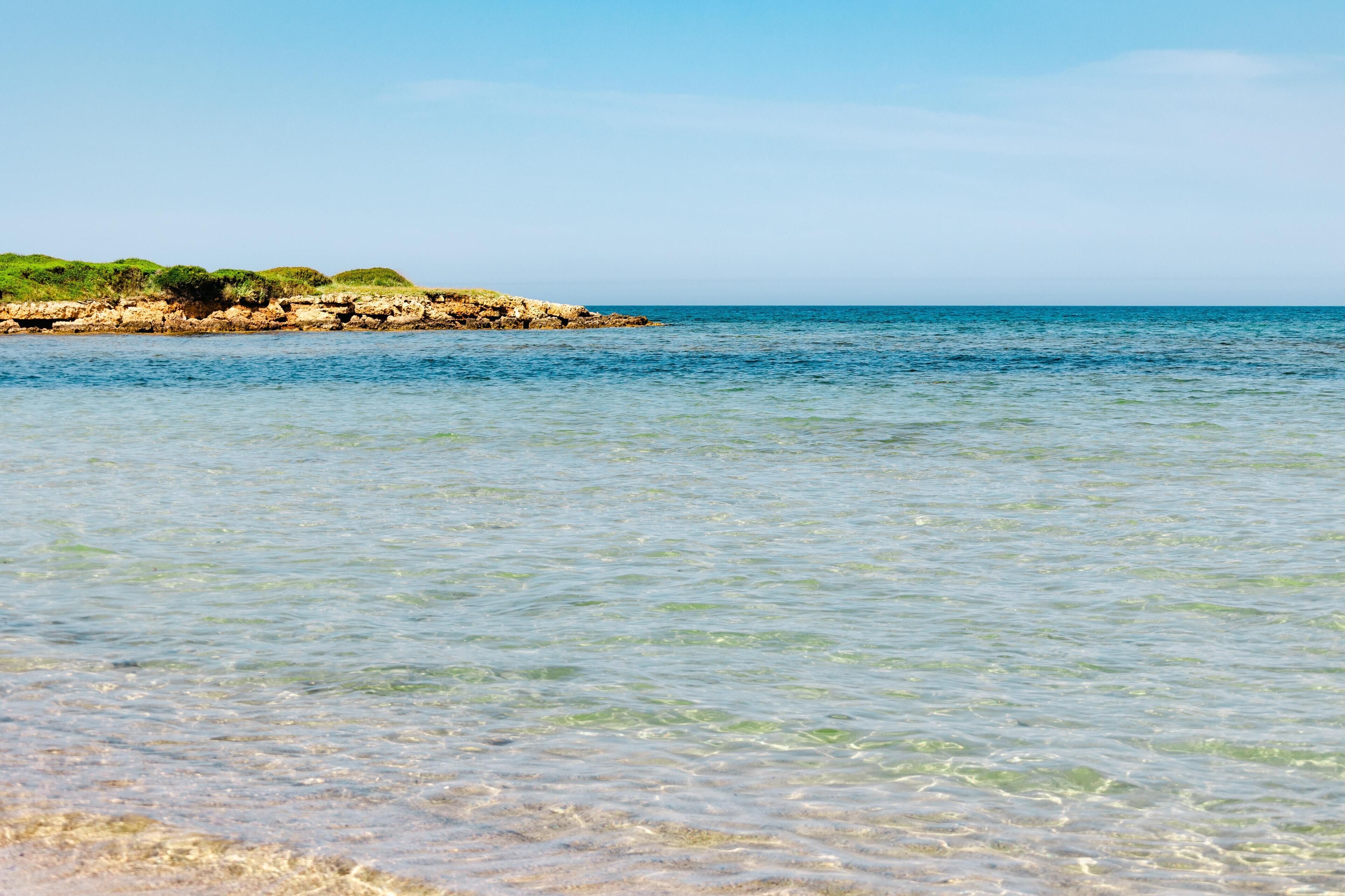 A coastal beach with clear water and a rocky shoreline.