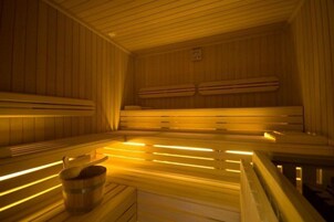 Una sauna con bancos de madera, un balde de madera y un calentador fijado a la pared.
