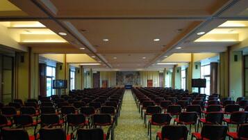 Ein Konferenzraum mit Reihen von Stühlen, einem Teppichboden und einer großen Leinwand im vorderen Bereich.
