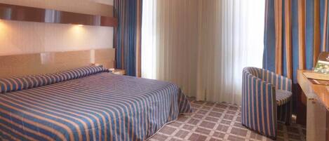 Una habitación de hotel con una cama, una silla, un escritorio y un televisor.
