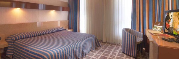 Una habitación de hotel con una cama, una silla, un escritorio y un televisor.