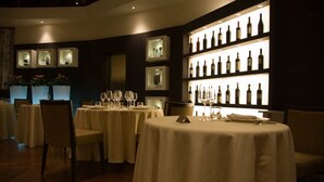 Un restaurante tenuemente iluminado con mesas redondas cubiertas con manteles blancos, cada una dispuesta con copas de vino y cubiertos.