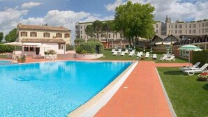 Una piscina con un deck de baldosas, sillones de descanso y una fuente.