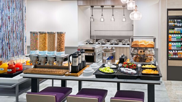 Ein Frühstücksbuffet mit verschiedenen Speisen und Getränken, einer Kaffeestation und Sitzbereichen.