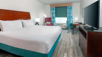 A hotel room with a large bed, a desk with a chair, a television, and a window with curtains.