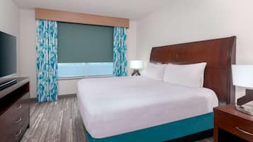 Ein Hotelzimmer mit einem großen Bett, einem Fernseher auf einer Kommode und einem Fenster mit Vorhängen.