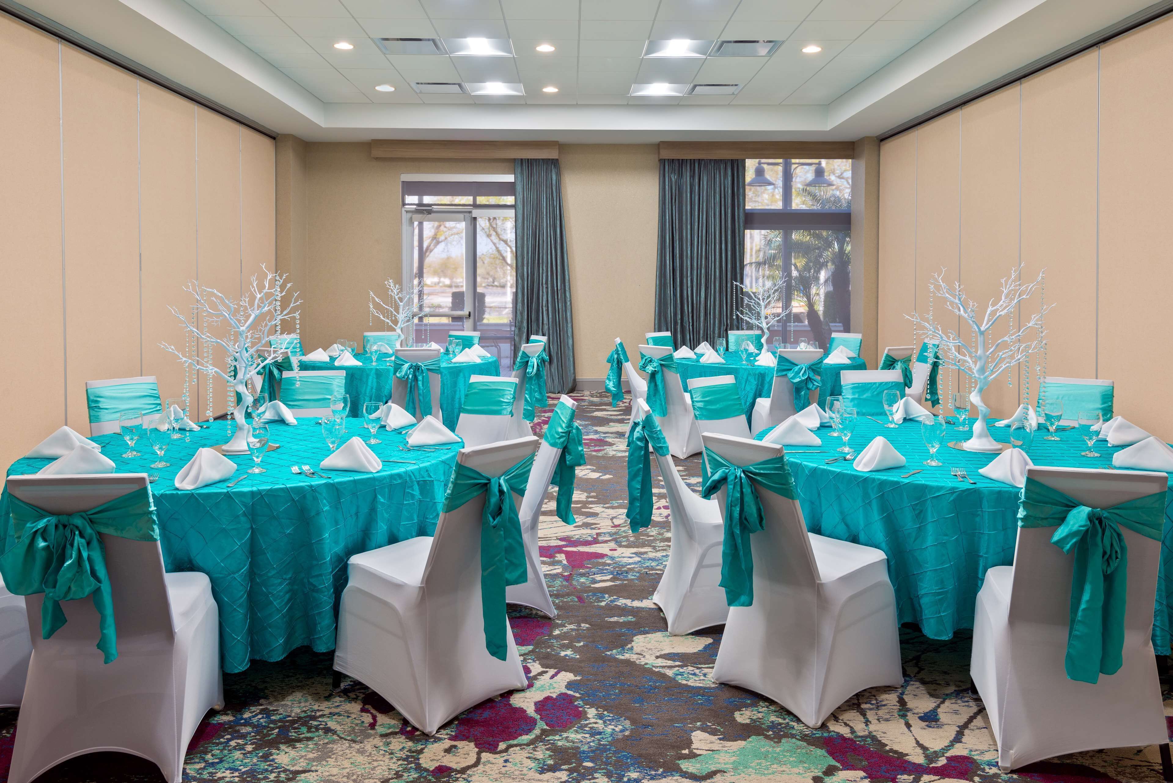 Un salón de conferencias con manteles color aguamarina, sillas blancas adornadas con cintas aguamarinas y centros de mesa blancos.