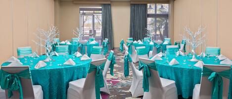 Un salón de conferencias con manteles color aguamarina, sillas blancas adornadas con cintas aguamarinas y centros de mesa blancos.
