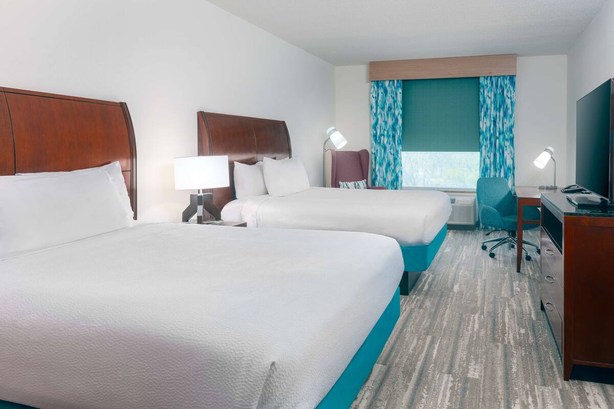Una habitación de hotel con dos camas, un escritorio, una silla y un televisor.