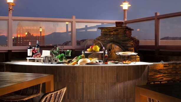 An outdoor bar area with a stone oven, wicker chairs, and a view of a cityscape at dusk. - DoubleTree by Hilton El Paso Downtown (El Paso)