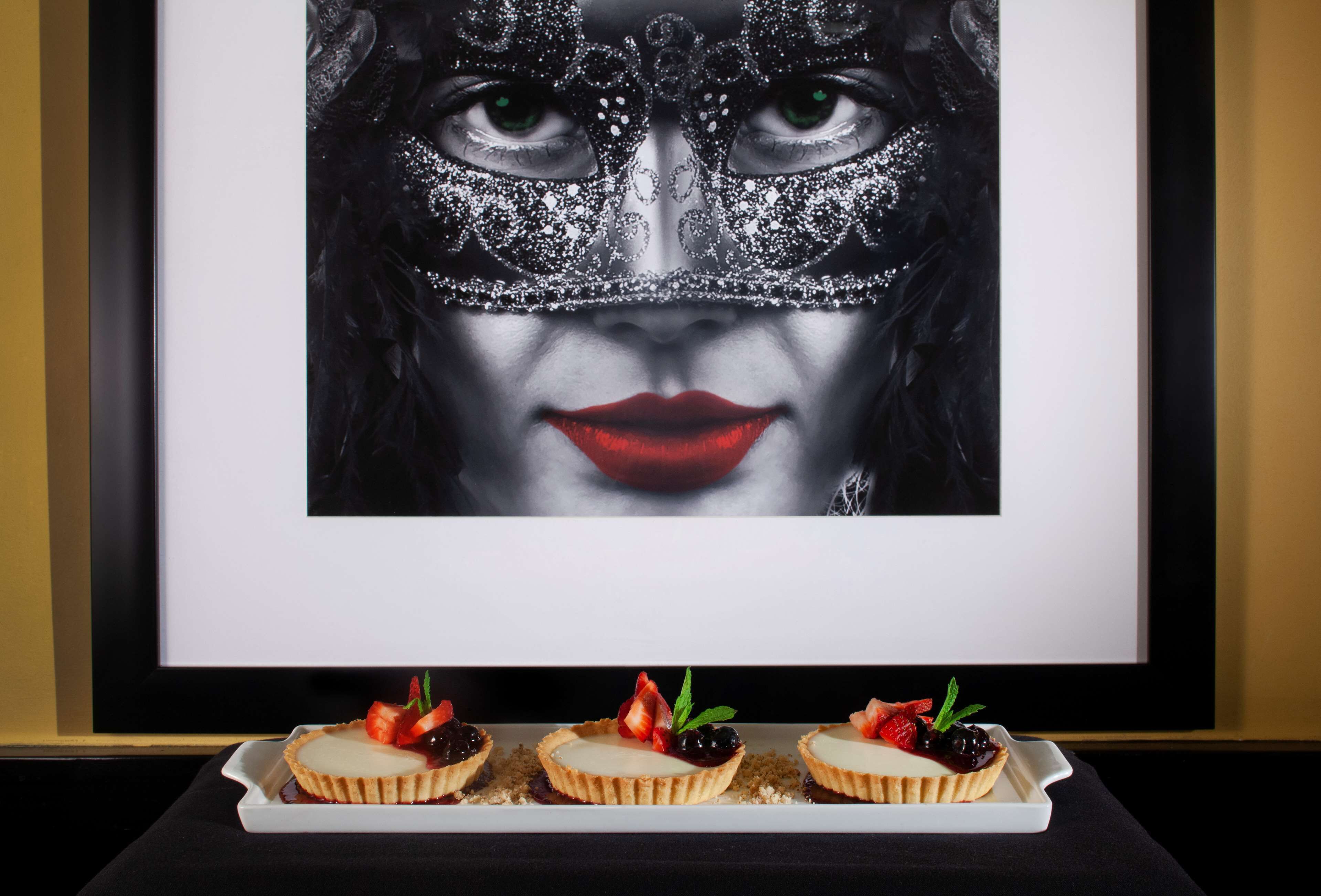 Une œuvre d’art encadrée, présentant un motif abstrait aux tons sombres, et un plateau avec trois desserts aux fraises et aux feuilles de menthe.