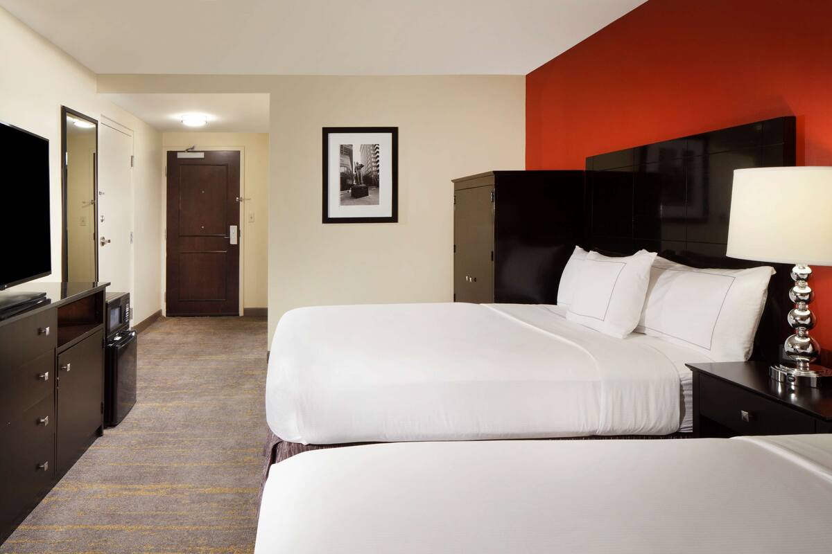 A hotel room with a large bed, a TV, a desk with a lamp, and a wardrobe.