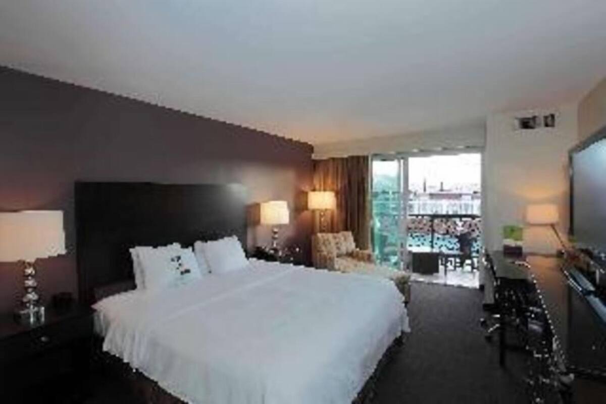 A hotel room with a bed, a desk, a chair, a TV, and a view of the city.
