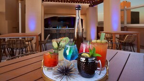 A table with various drinks and a bottle, set in an outdoor patio area with a bar in the background. - DoubleTree by Hilton El Paso Downtown (El Paso)
