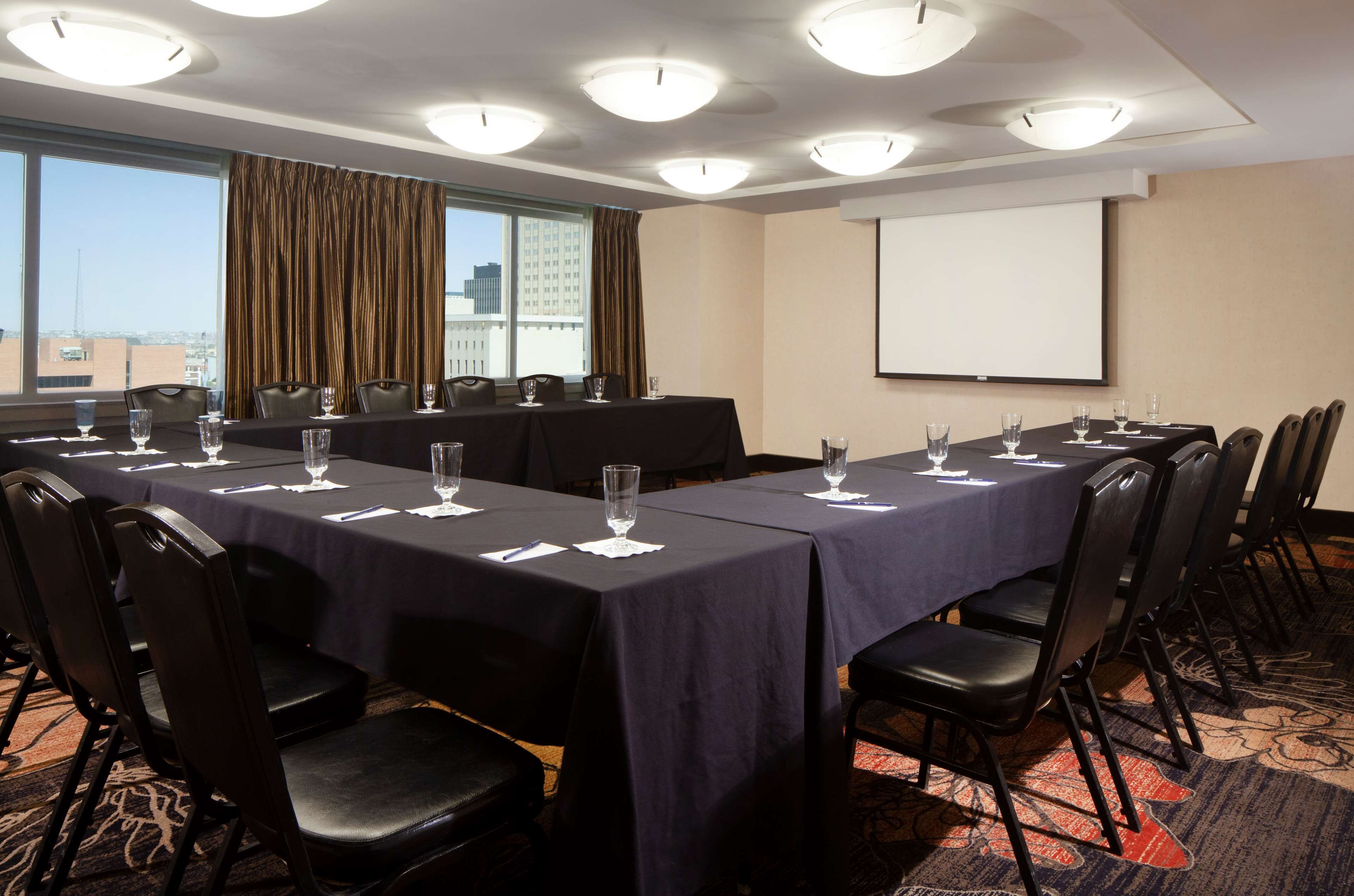 A conference room with a long table, chairs, a projector screen, and a view of the city through large windows.