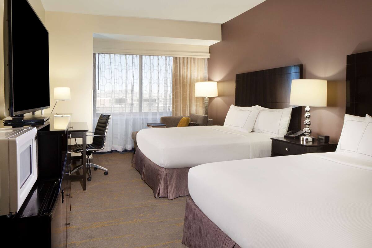 A hotel room with two beds, a desk with a computer, a TV, and two lamps.
