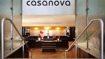 A hotel lobby with a reception desk, a staircase, and a sign that reads "casanova".