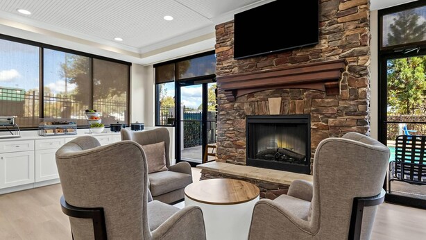 A modern living room with a stone fireplace, comfortable seating, and a kitchen area in the background. - Comfort Suites Augusta Riverwatch (Augusta)