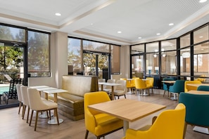 A modern indoor dining area with tables and chairs, large windows, and a view of the outdoors. - Comfort Suites Augusta Riverwatch (Augusta)