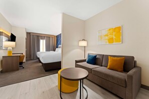 A hotel room with a bed, a sofa, a small table, a desk, and a lamp. - Comfort Suites Augusta Riverwatch (Augusta)