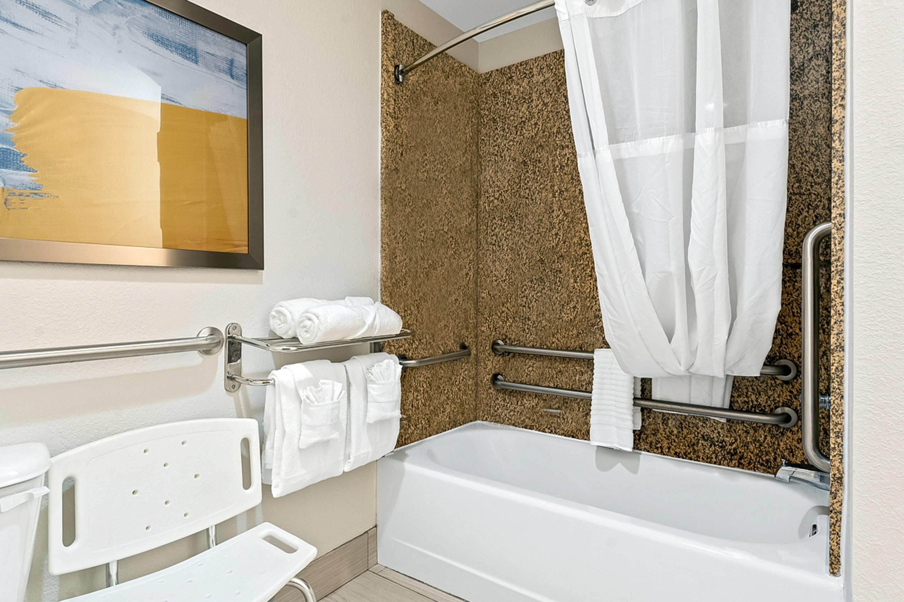 A bathroom with a bathtub, a shower with a textured wall, a handrail, and a towel rack.