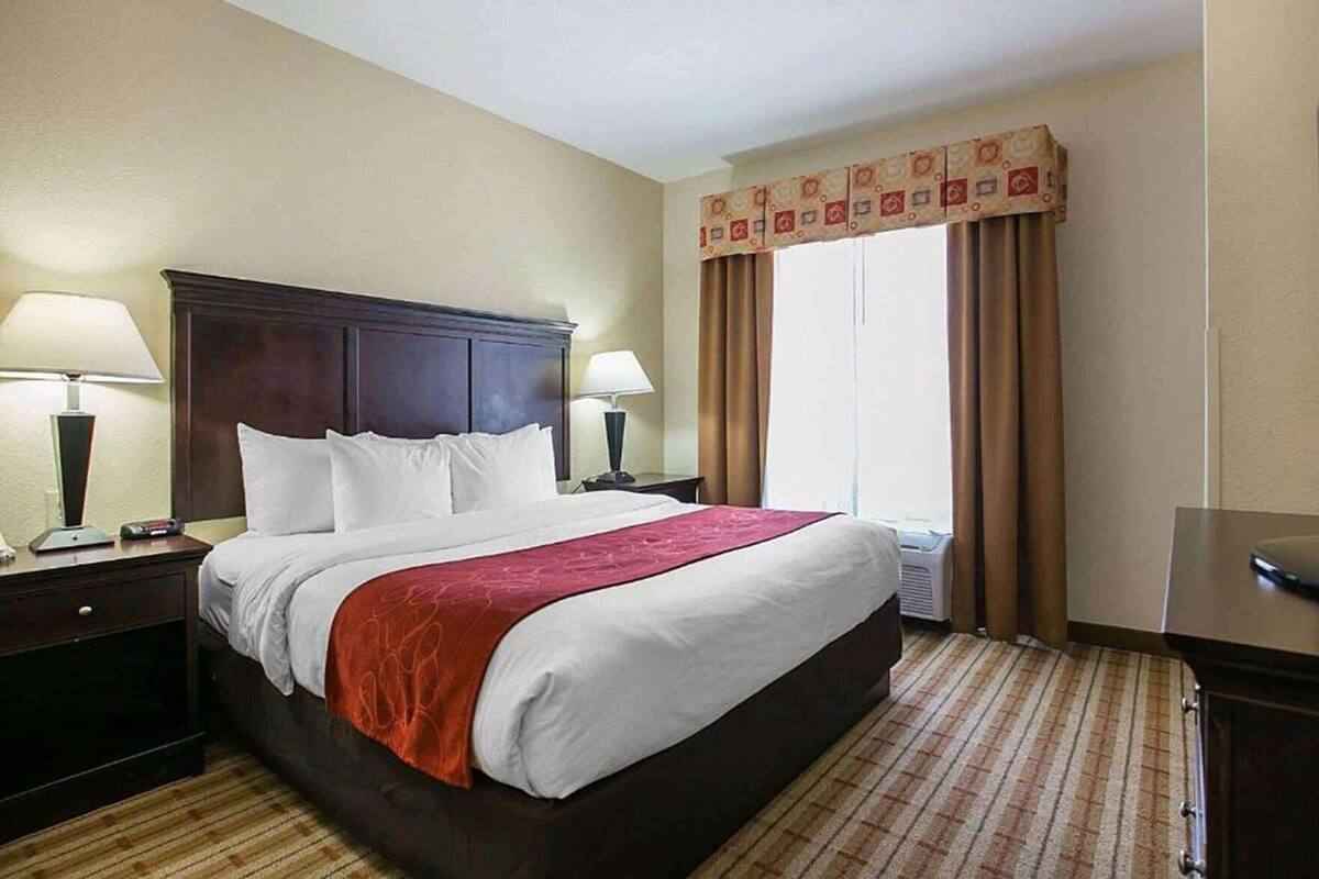 Habitación de hotel con una cama grande, dos mesitas de noche, un ventanal con cortinas y un equipo de aire acondicionado.
