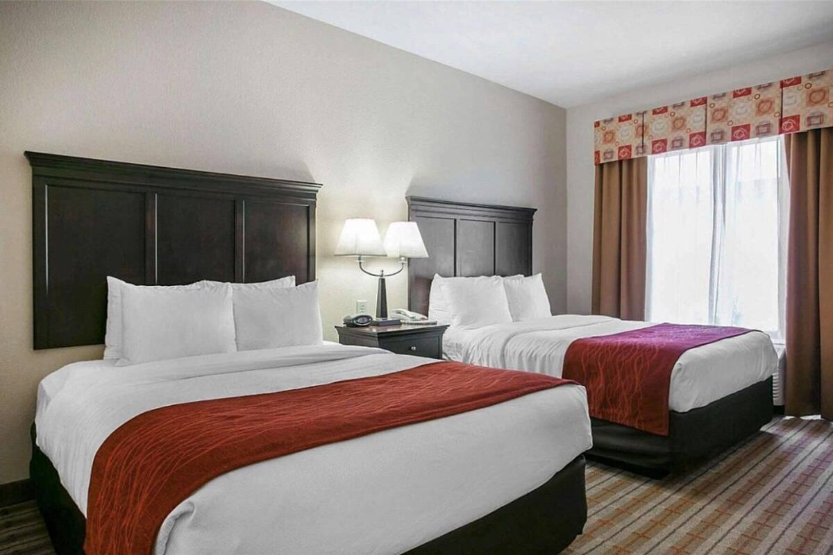 Una habitación de hotel con dos camas, una mesita de noche con lámparas y una ventana con cortinas.