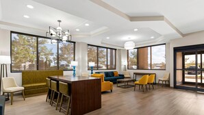 A modern hotel lobby with a wooden reception desk, yellow and blue chairs, a green sofa, and large windows offering a view of trees and parked cars. - Comfort Suites Augusta Riverwatch (Augusta)