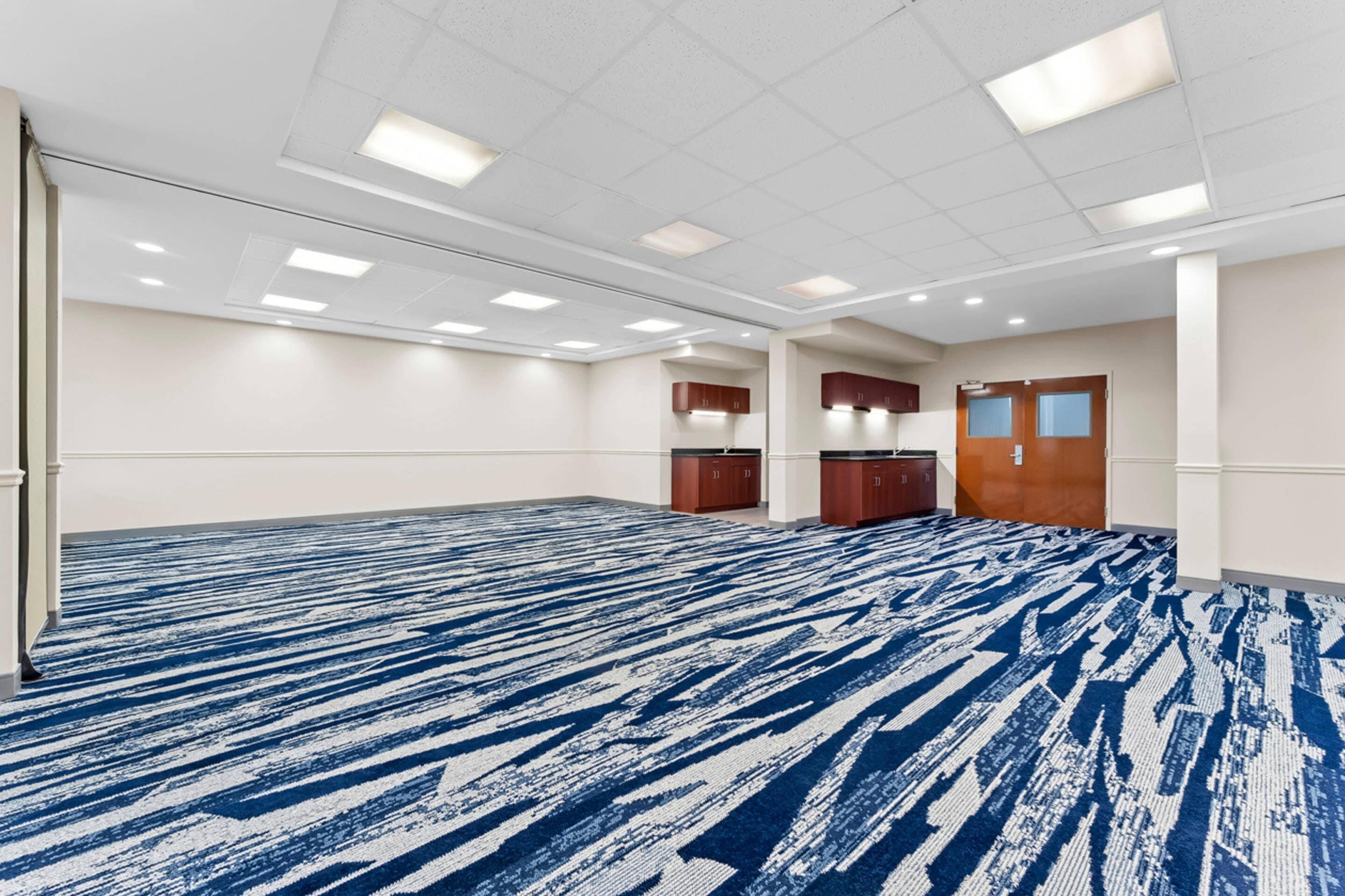 A large conference room with a patterned carpet, white walls, and wooden cabinets.
