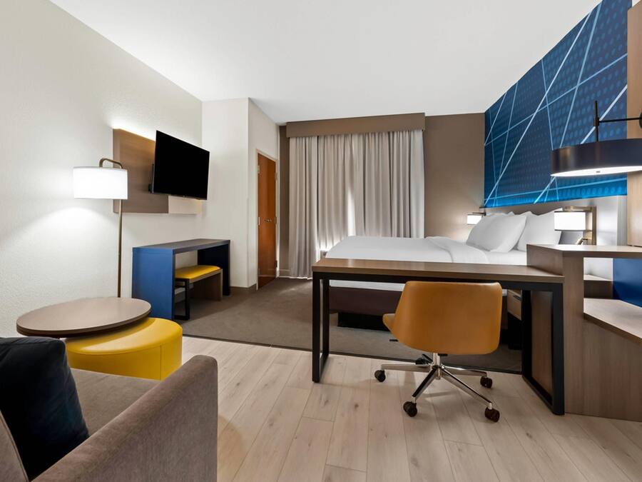 A hotel room with a bed, desk, chair, TV, and a large window with curtains.