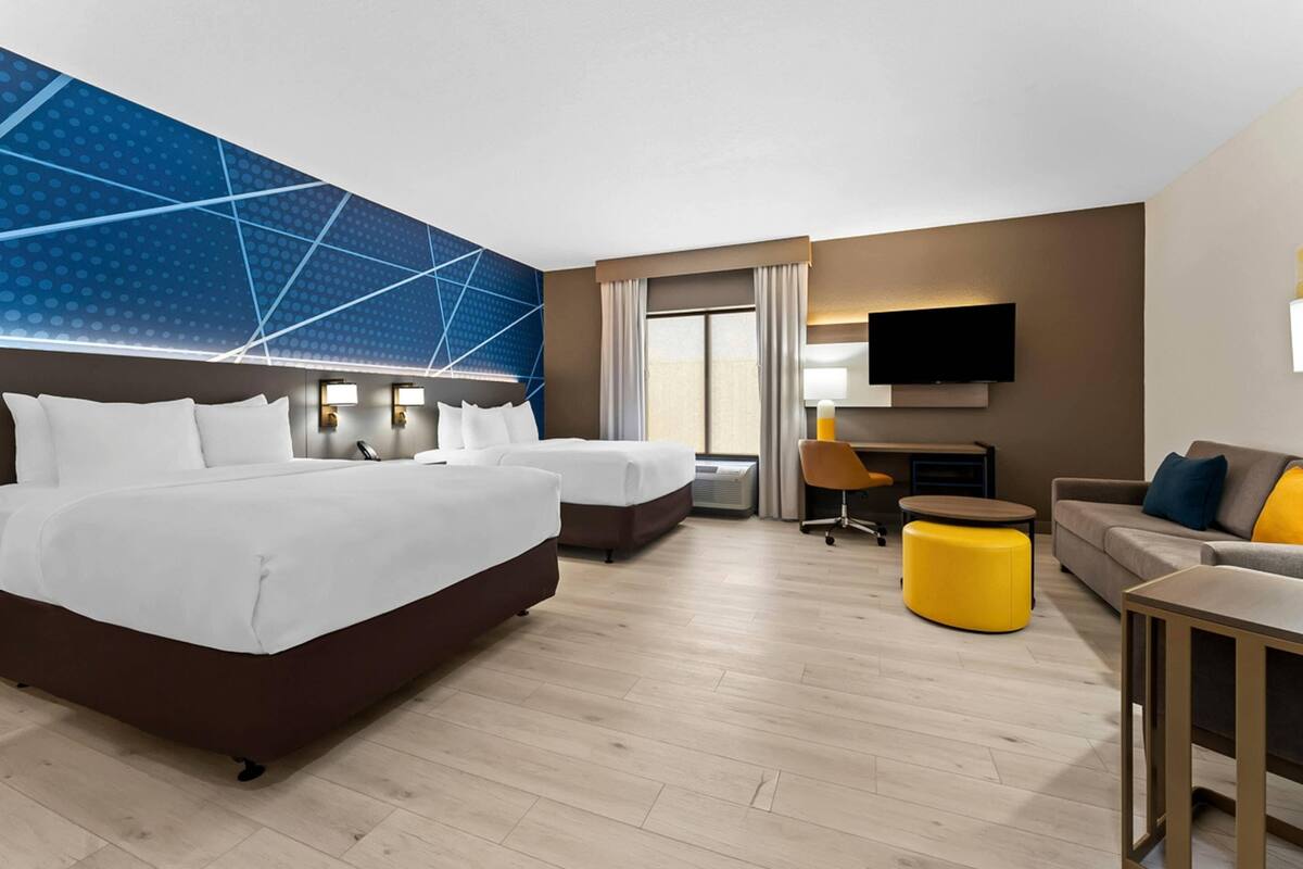 Habitación de hotel con dos camas, un sofá, una televisión y un escritorio.