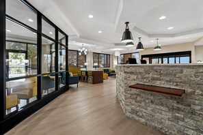 A modern interior with large windows, a stone accent wall, and a dining area with yellow chairs. - Comfort Suites Augusta Riverwatch (Augusta)