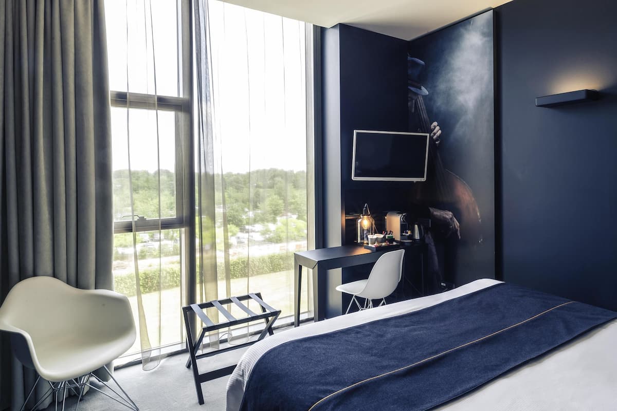 Ein modernes Hotelzimmer mit einem großen Bett, einem Schreibtisch, einem Stuhl und einem an der Wand befestigten Fernseher.