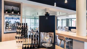 Una zona de bar con un enfriador de vino, botellas de vino y una copa de vino sobre una encimera.