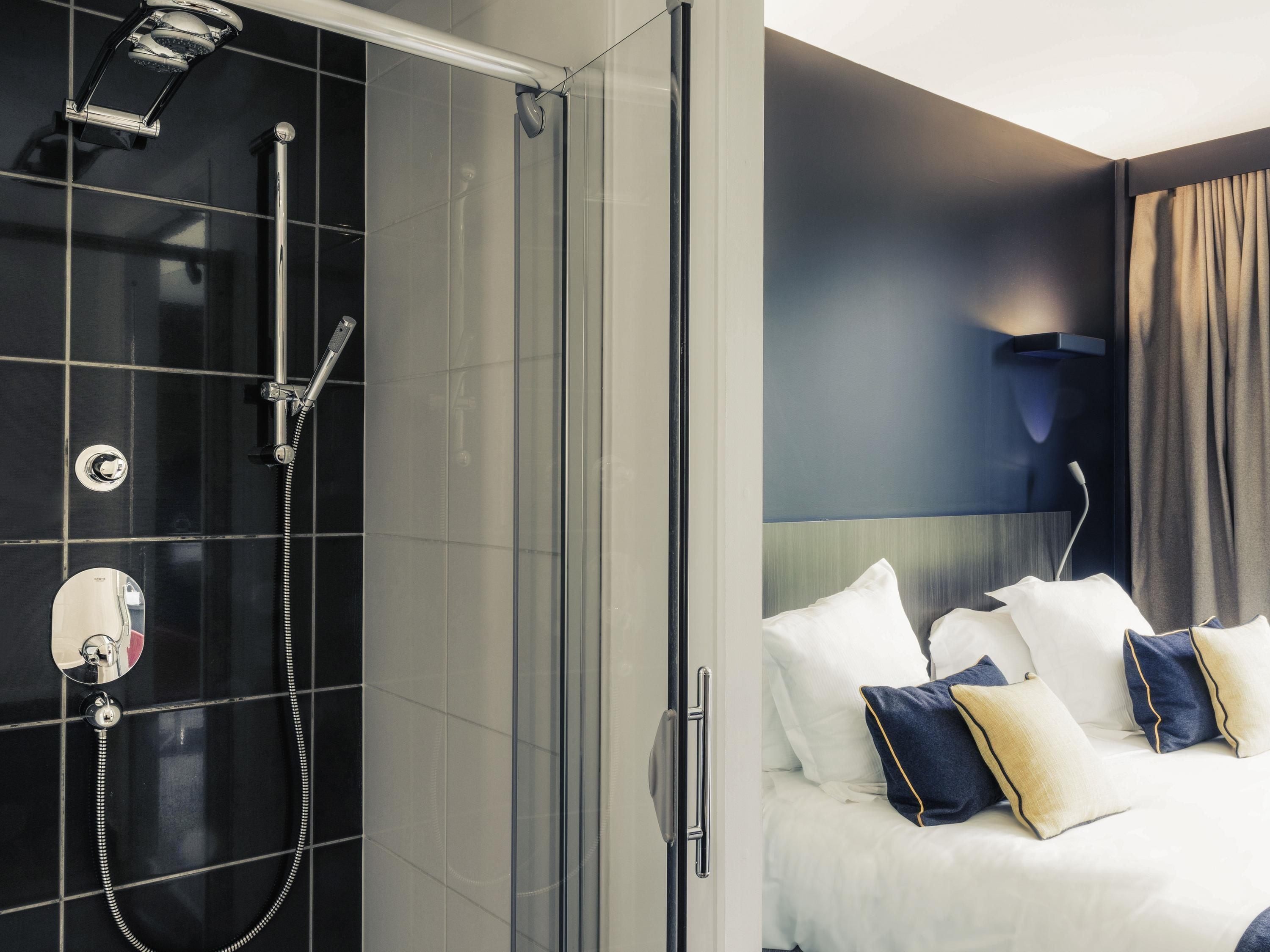 A hotel room with a shower, a bed with white bedding and navy pillows, and a modern wall-mounted light fixture.