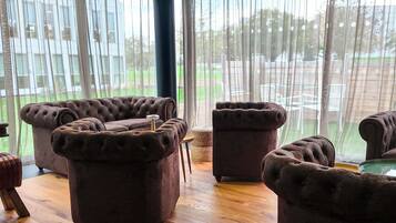 A room with large windows, a wooden floor, and multiple brown upholstered chairs.