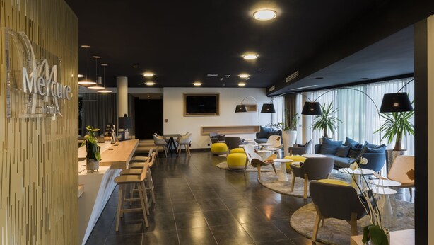 A modern hotel lobby with a reception desk, seating area with chairs and sofas, and a large window with curtains. - Hôtel Mercure Nantes Ouest Saint-Herblain Zenith (Saint-Herblain)